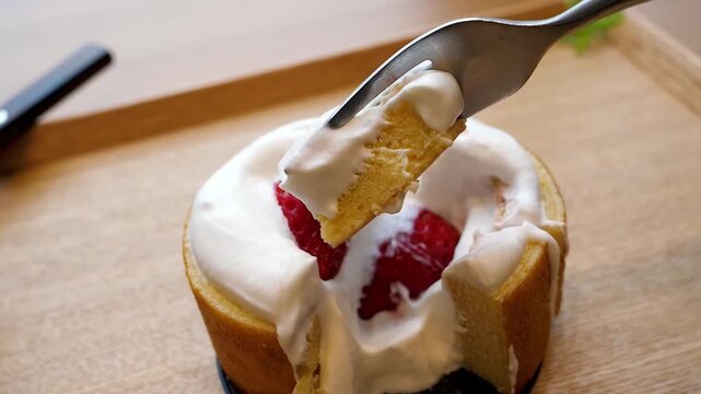 A close-up shot of a delicious, light, and fluffy strawberry chiffon cake. The cake is topped with fresh whipped cream and a whole red strawberry. A fork is shown taking a bite out of the cake, reveal