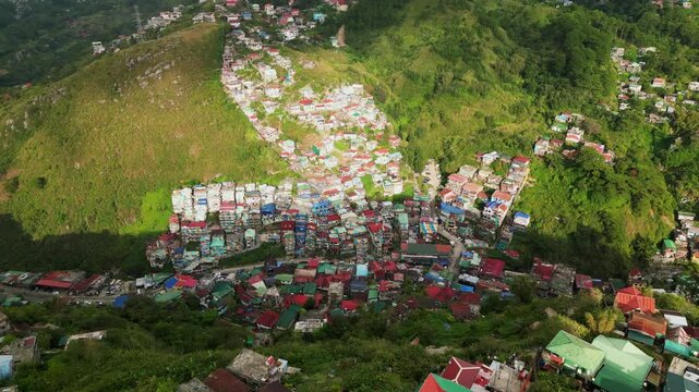 Panoramic orbiting aerial view of hillside village with colorful rooftops at lush valley - Baguio, Benguet, Philippines