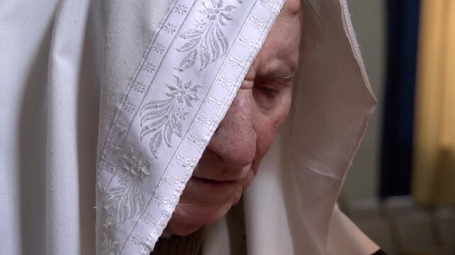 Elderly jewish man with a traditional tallit covering his head in a moment of deep prayer