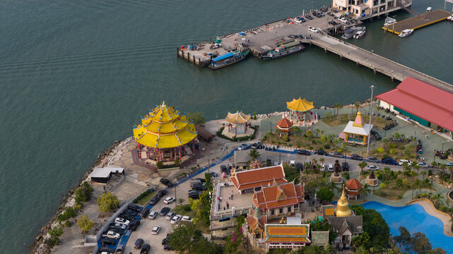 Aerial view of the colorful Koh Loy Temple with its yellow-roofed pavilion and the nearby pier on the coast of Si Racha, Chonburi, Thailand.