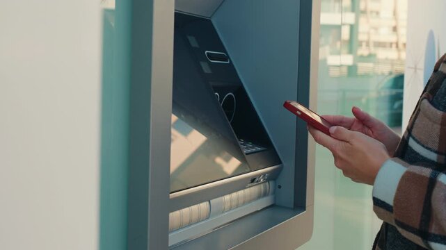 Woman using smartphone for contactless cash withdrawal at atm with nfc technology, facilitating modern, secure, and convenient electronic financial transaction.Cardless cash withdrawal, mobile banking