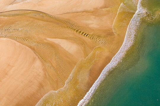 Aerial view of the intricate sand ripple patterns and turquoise water along the coastline in Erquy, Brittany, France.