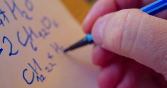 A marker writes a chemical formula on a piece of paper. Close-up. Shallow depth of field.