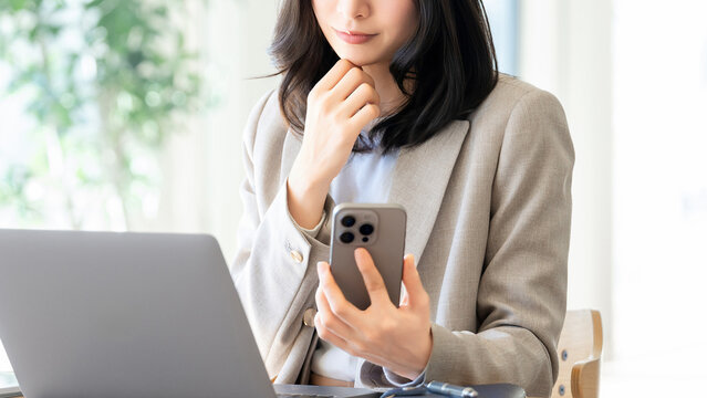 スマートフォンを持ちながら考える女性ビジネスパーソン, Businesswoman thinking while holding smartphone