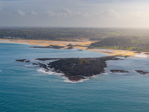 Aerial view of the rocky Ilot Saint-Michel and the sandy beaches along the coastline under a soft sky in Erquy, Brittany, France.