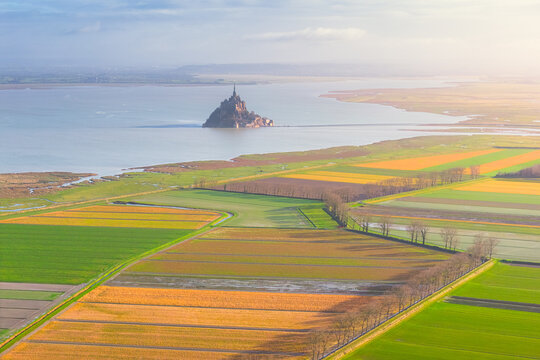 Aerial view of the historic Mont Saint-Michel abbey on its tidal island across colorful agricultural fields in Mont Saint-Michel, Normandy, France.