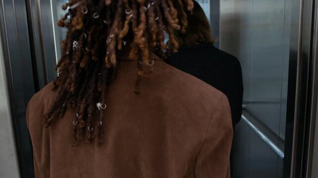 Handheld shot of gen Z multiethnic couple of business partners or coworkers wearing suits entering elevator cabin in modern office building