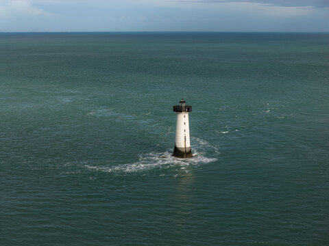 Aerial view of the Phare de la Pierre-de-Herpin lighthouse surrounded by turquoise waters and gentle waves in Cancale, Bretagne, France.