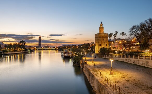 View over the river Rio Guadalquivir with Torre del Oro, promenade and Puente de Triana, in the back Torre Sevilla, sunset, blue hour, Sevilla, Andalusia, Spain