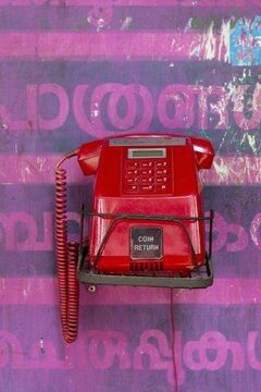 Old red telephone against a wall with pink Malayalam script, Kerala, India