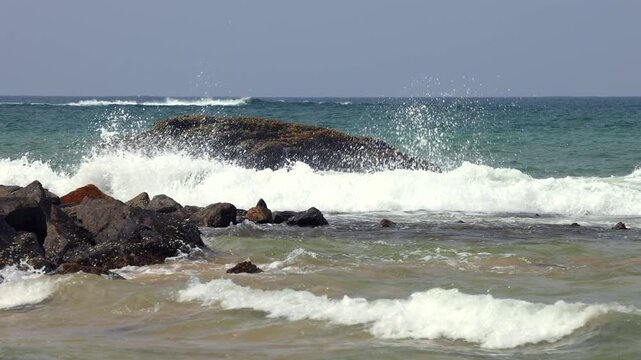 Ocean Waves Crash Against Rocky Shoreline, Water Splashes Over Coastal Rocks on a Sunny Day, Nature's Power at the Beach. Sri Lanka island in Asia.