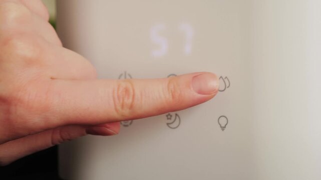 A hand sets the humidity level on a humidifier at home. A modern humidifier that produces cool water vapor to moisturize the air in home and prevent respiratory infections. High quality 4k footage