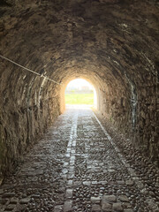 Fototapeta premium Stone tunnel and cobblestone path inside Corfu island New Fortress, Greece. Bright day light at the exit