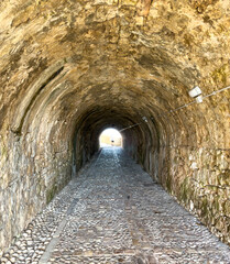 Fototapeta premium Stone tunnel and cobblestone path inside Corfu island New Fortress, Greece. Bright day light at the exit