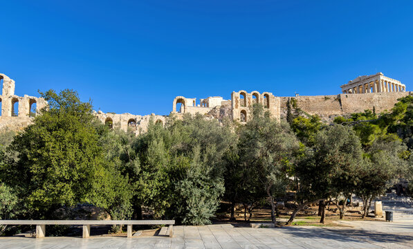 Parthenon temple and the herodeion rise above olive trees in Acropolis hill in Athens, Greece. Blue sky