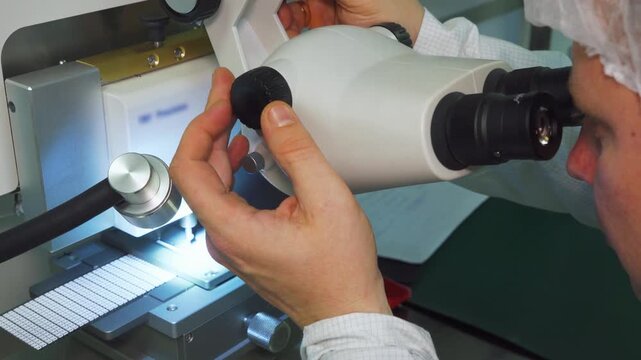 Precision technician analyzing microchip within sterile laboratory environment. Skilled professional conducting detailed microelectronic test using advanced microscopy tools in cleanroom setting