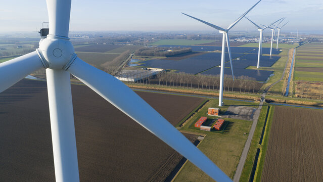Aerial view of modern wind turbines and a large solar farm situated in flat agricultural fields under a clear blue sky.