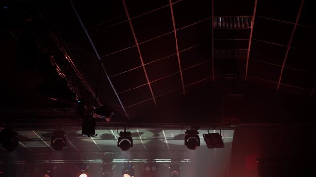 Dynamic video showing multiple stage lights activating and intensifying, casting red and orange hues on a dark ceiling grid, building atmosphere for a concert or performance