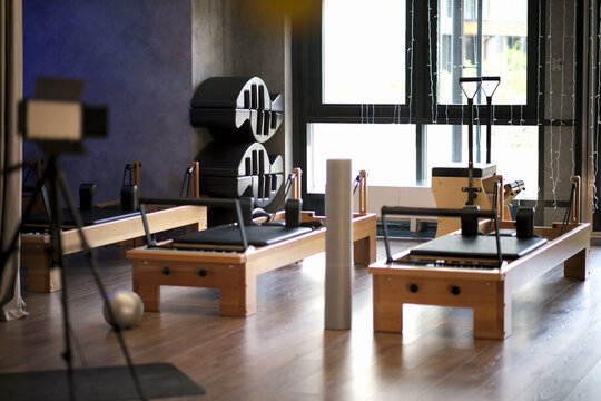 A quiet Pilates studio with reformers, foam roller, and props is shown in soft daylight from a wide interior angle. The clean room suggests mindful workouts, recovery, and modern wellness habits.