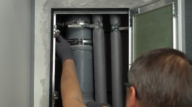 Plumber installs and repairs sewer pipe in hidden technical inspection hatch in wall. Sewerage. Water pipes
