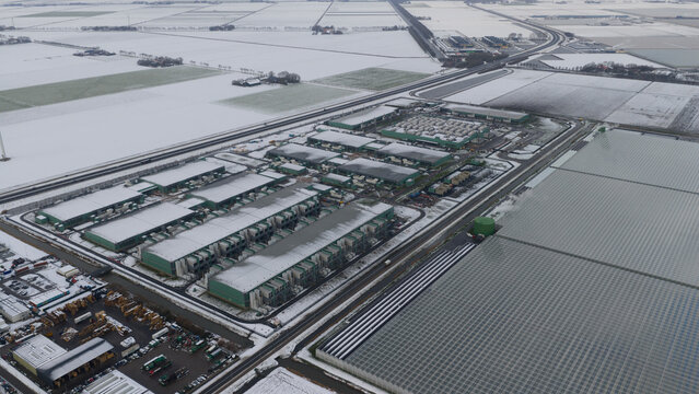 Aerial view of the Agriport a7 datacenter complex and large greenhouses surrounded by snow-covered fields in Middenmeer, Noord-Holland, Netherlands.