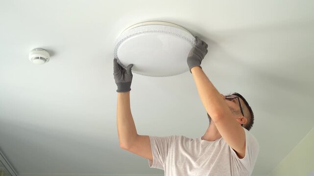 Electrician installs ceiling LED lamp on suspended ceiling. Hands connect and fix lampshade. Installation light