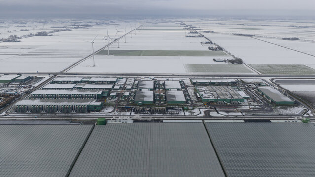 Aerial view of the Agriport A7 datacenter complex surrounded by snow-covered fields and wind turbines in Middenmeer, Noord-Holland, Netherlands.
