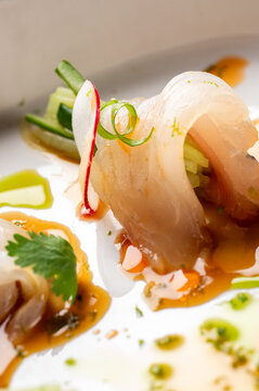 A close-up shot of yellowtail hamachi crudo sashimi, elegantly rolled with julienned cucumber, garnished with radish slices, scallions, and cilantro, served with a citrus yuzu soy sauce.
