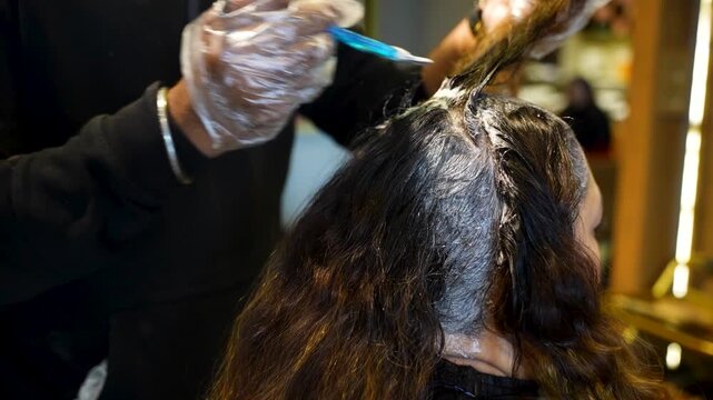 Hair stylist applying bleaching product to sectioned hair during coloring treatment in beauty salon