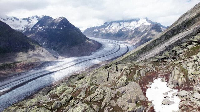 Aerial 4k drone view of Aletsch alpine glacier and mountain valley with hikers resting on rocky trail, showcasing glacial curves, moraines, adventure travel, and climate‑impacted ice formations