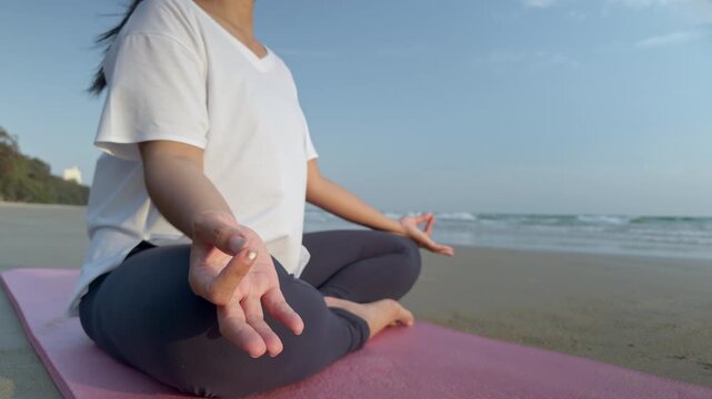 Close up of woman practicing yoga meditation on beach at sunrise. Focus on hands in mudra gesture, calm ocean background, mindfulness, relaxation and mental health concept.