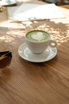 Woman hands holding cup of green matcha latte at sunlit cafe table with notebook, aesthetic morning routine and mindfulness concept
