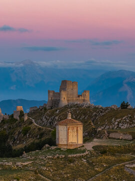 Aerial view of the historic Rocca Calascio fortress and Santa Maria della Pieta chapel on a mountain ridge during sunset in Calascio, Abruzzo, Italy.