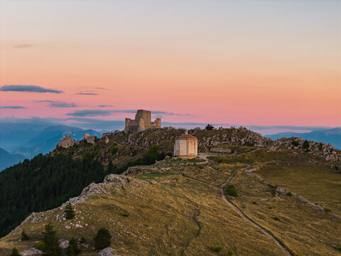 Aerial view of the medieval Rocca Calascio fortress and Santa Maria della Pieta chapel on a mountain ridge at sunset Calascio, Abruzzo, Italy.