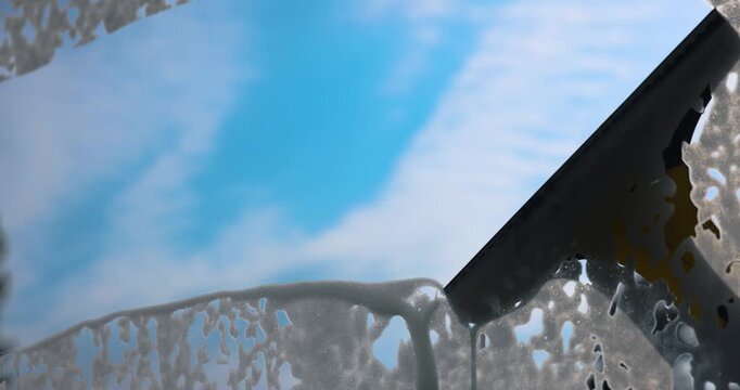 hand washes window glass with vacuum squeegee cleaner against blue sky