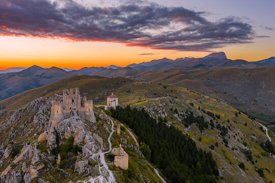 Aerial view of Rocca Calascio and the church of Santa Maria della Pieta perched on a rocky ridge overlooking the Apennine Mountains during a vibrant sunset Calascio, Abruzzo, Italy.