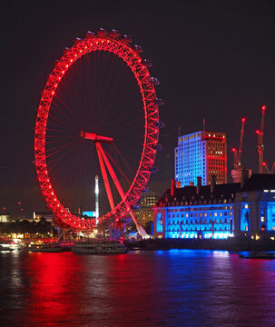  The London Eye Ferris wheel, colorfully illuminated at night, is reflected in the River Thames
