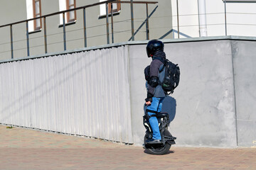 Rider on unicycle navigating modern urban space with safety gear and backpack, personal electric vehicle. Man in protective equipment riding electric unicycle along paved city road © Tricky Shark