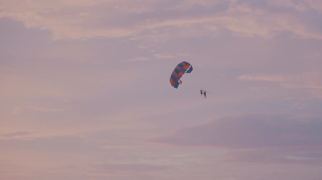 Sunset parasail over open ocean sky, colorful chute suspending lone adventurer in pastel dusk, calm drift above distant island silhouette, serene leisure vibe, cinematic golden hour travel footage