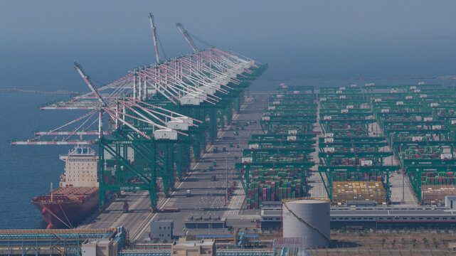 Fengsen Village, Taiwan - 26 February 2026: Aerial view of the Port of Kaohsiung featuring rows of green gantry cranes, a docked container ship, and vast stacks of shipping containers by the sea.