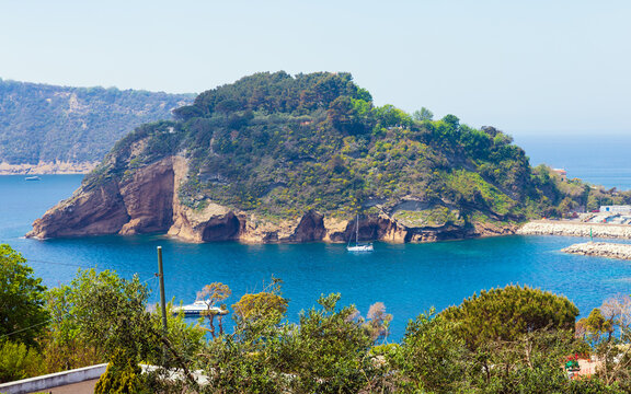 Scenic coastal landscape of Procida, Italy. Rugged island with steep cliffs and green dense vegetation surrounded by blue waters of Mediterranean Sea