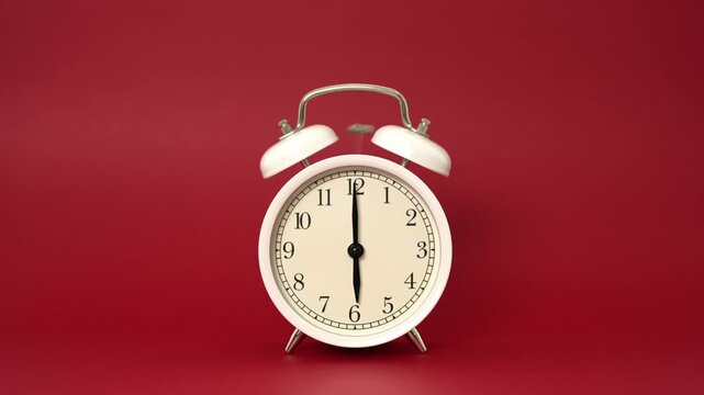 Classic white twin bell alarm clock ringing loudly at six o'clock, creating vibrations and jumping on a vibrant red background, symbolizing the urgency to wake up and start the day