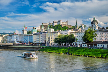 Obraz premium Sightseeing boat cruising on the Salzach river with the historic Salzburg city center and fortress on the hill, Salzburg, Austria.
