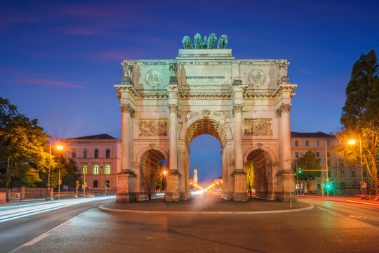 Dramatic twilight view of the Siegestor monument in Munich, Bavaria, Germany, featuring vibrant light trails from passing cars.