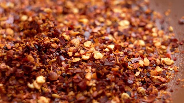 Chef taking a pinch of dried crushed red chili and cayenne pepper flakes from a wooden bowl