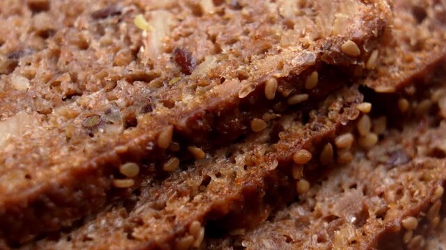 Macro view of stacked multigrain bread slices covered in toasted sesame seeds. Rotation