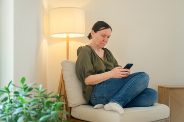 Obraz premium Woman sitting and checking phone in cozy living room