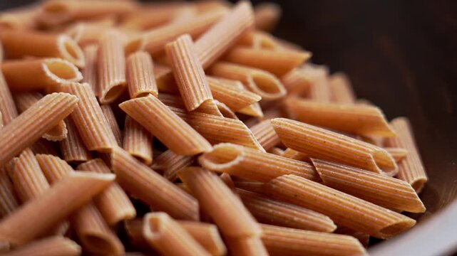 Close up of dry whole grain penne pasta in wooden rustic bowl. Healthy eating concept. Nutritious ingredient of high fiber food