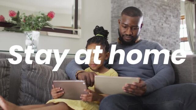 Animation of stay at home text over african american father and daughter using tablets