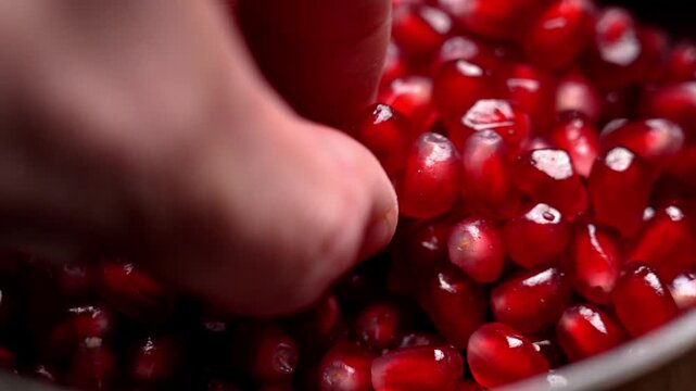 Human fingers picking pomegranate seeds from a bowl. Juicy translucent arils with glossy surface and natural moisture. Organic plant based diet ingredient.